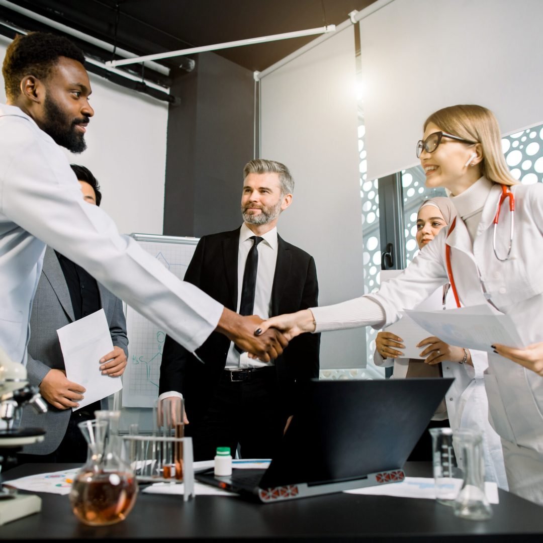 Handshake of female Caucasian and male African doctors, having a brainstorm or meeting with team of multiethnic colleagues. Concept of health, partnership and cooperation